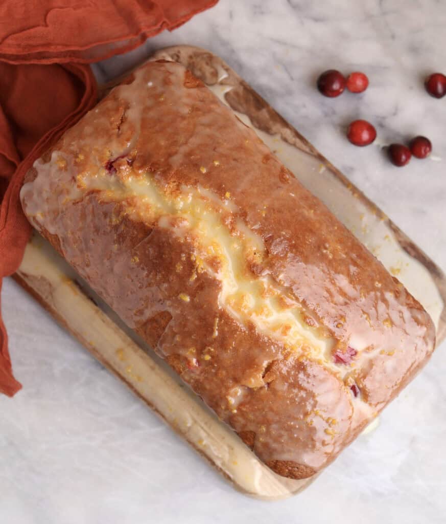 Orange cranberry bread on a cutting board with orange glaze.