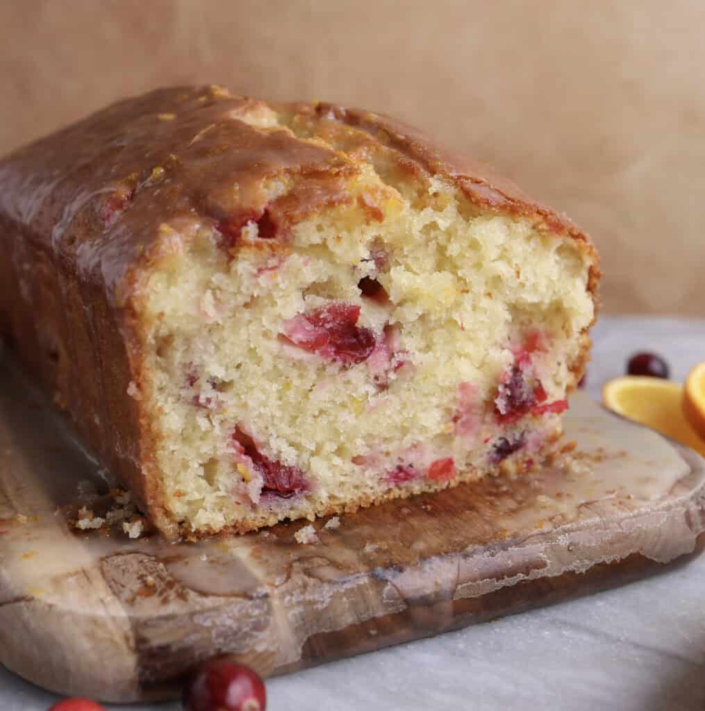 Cranberry orange bread on a cutting board sliced open, showing the cranberries inside the bread.