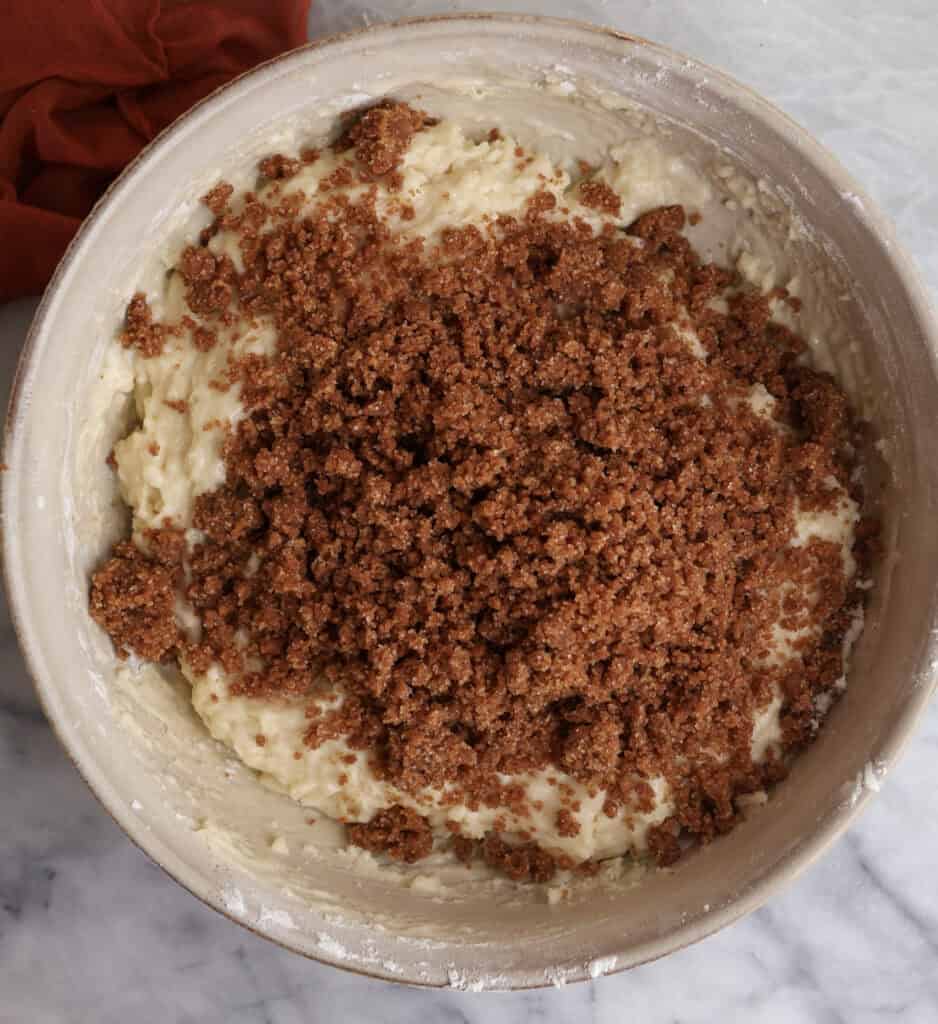 The cinnamon roll muffin batter in a large bowl with the cinnamon sugar mixture sitting top before being folded into the batter.