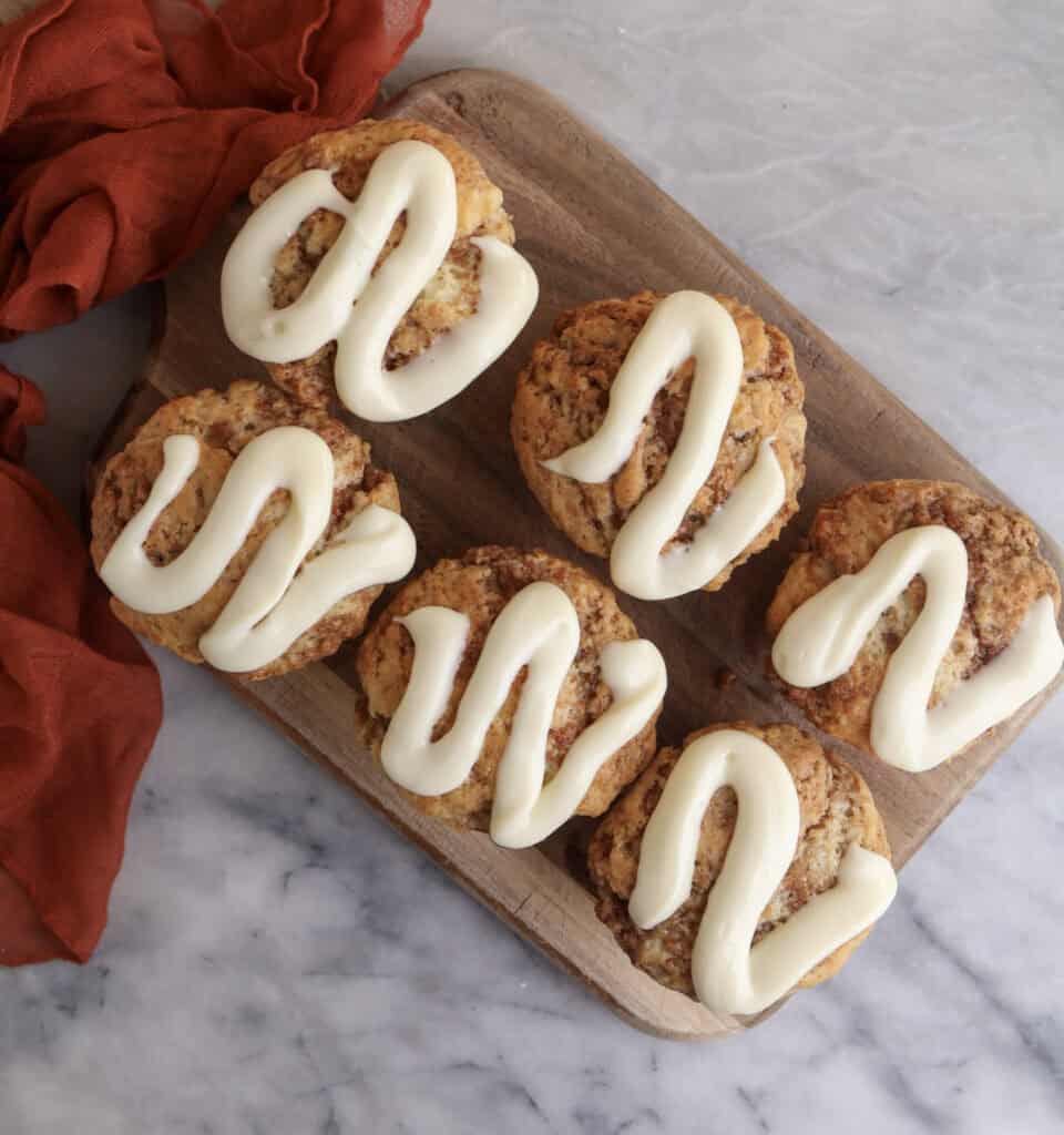 Cinnamon Roll muffins with cream cheese icing sitting on a wood cutting board.