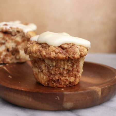 A cinnamon roll muffin with cream cheese icing sitting on a wood plate.