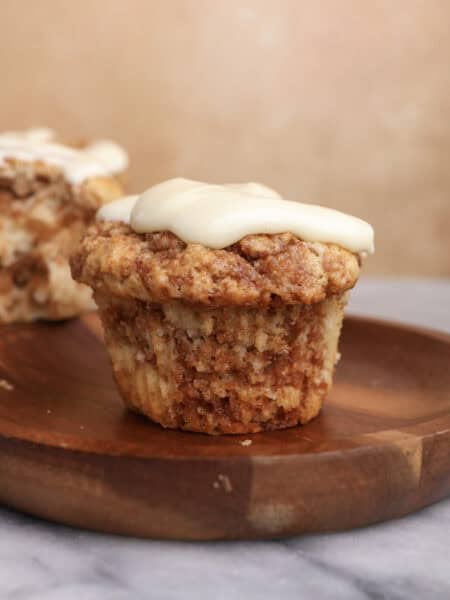 A cinnamon roll muffin with cream cheese icing sitting on a wood plate.