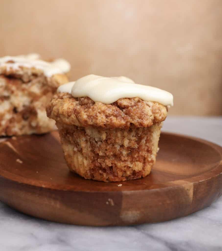A cinnamon roll muffin with cream cheese icing sitting on a wood plate.